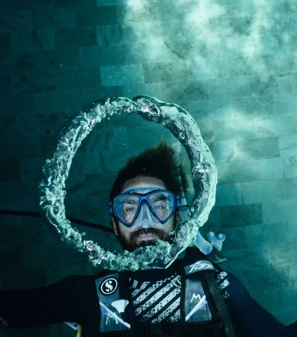 Buceador en Nusa Penida sopla un anillo de burbujas alrededor de su cara mientras está sumergido con máscara y equipo de buceo.